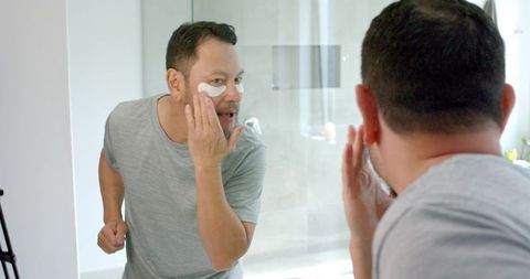 Asian man applying skincare patch in bathroom mirror