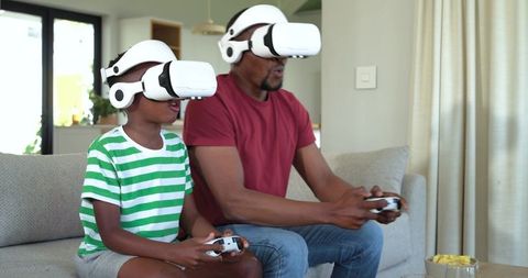 African American father and son playing virtual reality games on couch with controllers