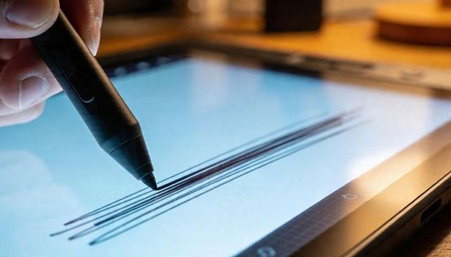 Drawing parallel lines with stylus on tablet screen showing fingertip and warm desk glow