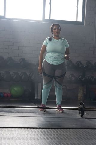 African american woman standing by barbell in gym wearing mint activewear for strength training