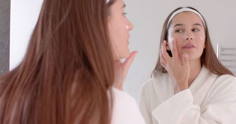 Woman Applying Moisturizer in Bathroom Mirror Skincare Routine