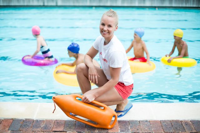 Portrait of female lifeguard holding rescue can while children swimming in pool