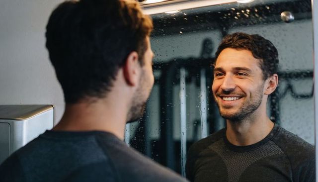Smiling man checking mirror reflection in locker room with water droplets and dispenser