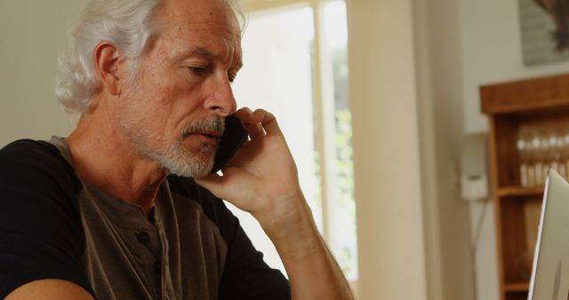 Senior Man Using Laptop and Talking on Smartphone at Home - Download Free Stock Images Pikwizard.com