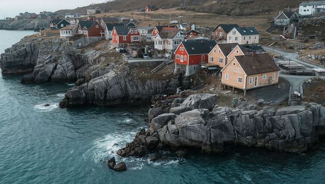 Colorful coastal fishing cottages perched on granite cliffs above dark teal ocean