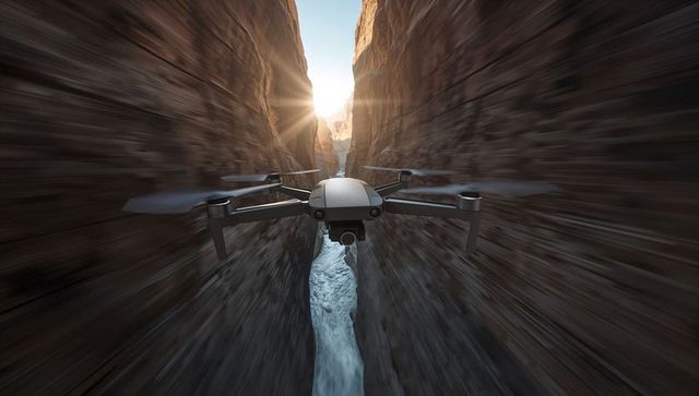 Quadcopter navigating narrow slot canyon over rushing river at sunrise with sun flare