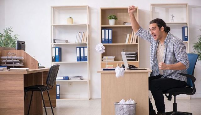 Young professional celebrating success at desk throwing crumpled paper into bin