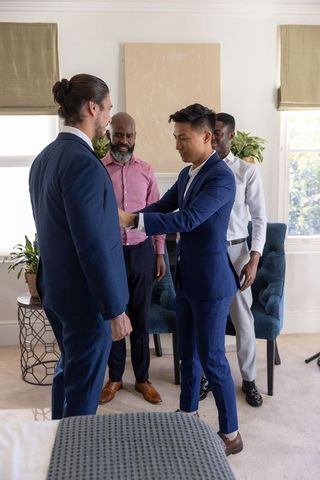 Groomsmen adjusting navy suits and cufflinks while preparing for wedding in bedroom