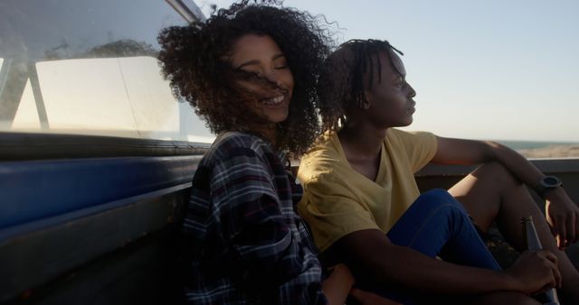 Friends sit in the back of a pickup truck enjoying a road trip during sunset. Photographed during golden hour, the image captures a relaxed moment. Perfect for ads and articles about travel, friendship, leisure activities, vacations, and the joyous essence of youth.