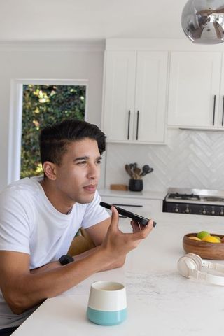 African american man speaking into smartphone on kitchen countertop, modern home lifestyle