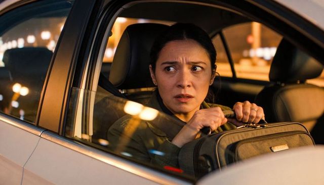Anxious woman gripping suitcase inside parked car at night with glowing safety hud on glass, urban