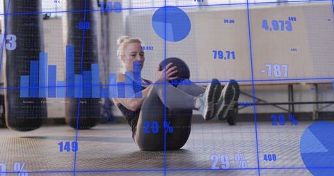 Female athlete performing medicine ball v-sit core workout in boxing gym with blue data overlay