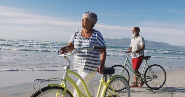 Smiling senior african american couple walking with bicycles at the beach - Download Free Stock Photos Pikwizard.com