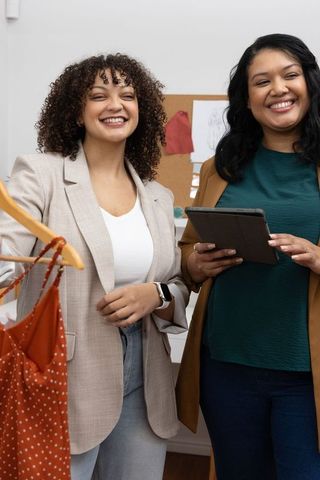 Diverse female boutique team presenting polka dot dress while consulting tablet