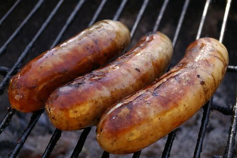 Three juicy sausages grilling on charcoal grill with golden brown skin and grill marks