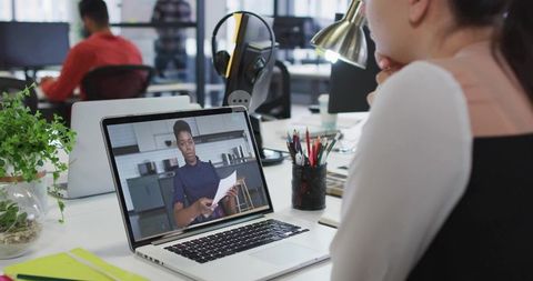 Watching remote presenter on laptop during office workday in modern open-plan coworking space