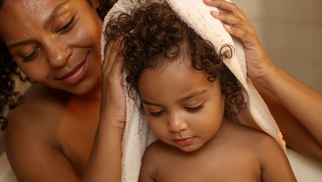Mother gently drying toddler's curly hair with towel during warm bath bonding moment