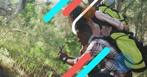 Couple hiking in sunlit woodland checking smartphone for navigation with lime green backpacks