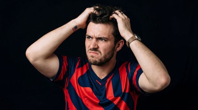 Frustrated young man gripping hair wearing red navy sports jersey, expression closeup