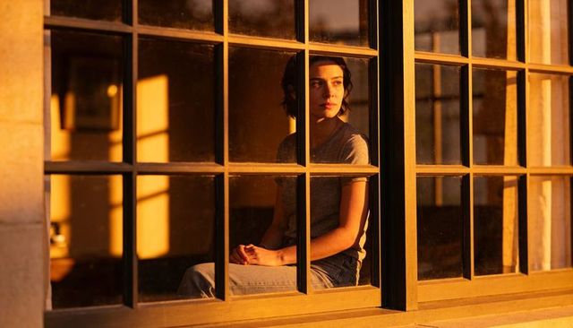 Woman gazing through multi-pane wooden window during golden hour, contemplative portrait