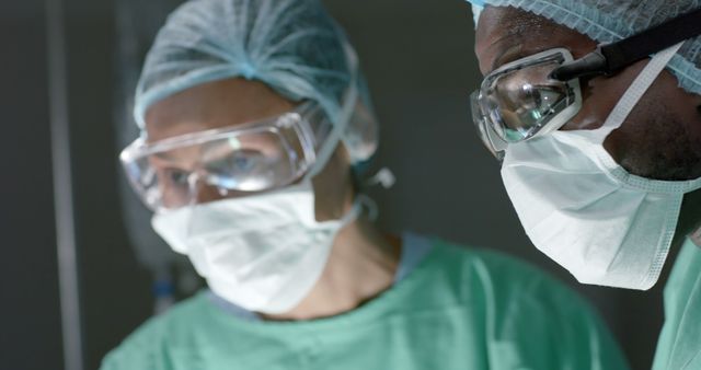 Focused diverse surgeons wearing face masks during surgery in operating room. Medicine, healthcare and hospital, unaltered.