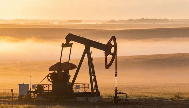 Sunrise pumpjack silhouette operating on misty prairie with wellhead and piping