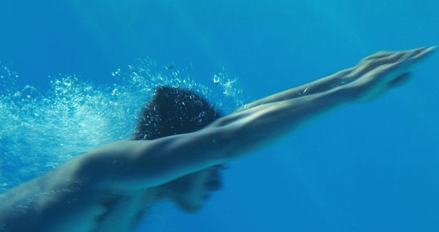 Person gliding underwater with streamlined arms in a swimming pool. Vivid blue water and motion create dynamic atmosphere. Ideal for themes of fitness, swimming, sport, aquatic activities, health and motion capture.
