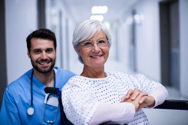 Portrait of male doctor and female senior patient smiling in the corridor at hospital 
