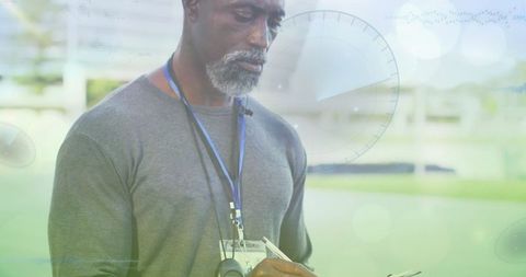 Mature Coach Analyzing Metrics on Clipboard in Athletic Field