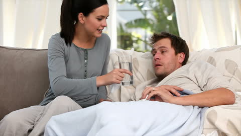 Caring Woman Assisting Sick Partner on Sofa with Pills