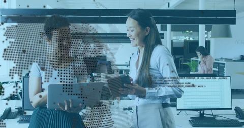 Women Comparing Tablets in Modern Open-Plan Office with Code and World Map Overlay
