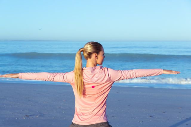 Caucasian woman wearing sports clothes, enjoying time at the beach on a sunny day, practicing yoga, arms stretched.