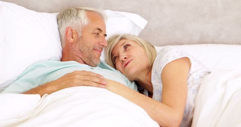 Senior couple lying in bed cuddling and talking