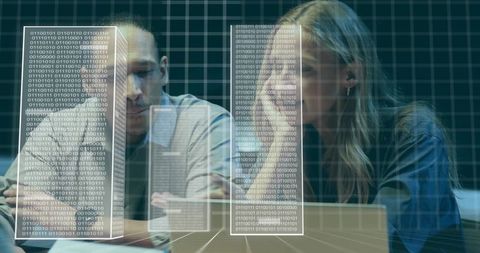 Two coworkers analyzing holographic binary dashboards on laptop in dim tech lab workspace