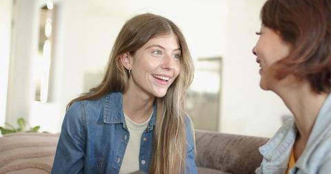Sunlit friends laughing and chatting on couch in modern living room, denim casual conversation