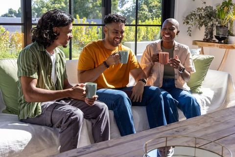 Close friends enjoying coffee on sunlit sofa sharing laughter and relaxed conversation