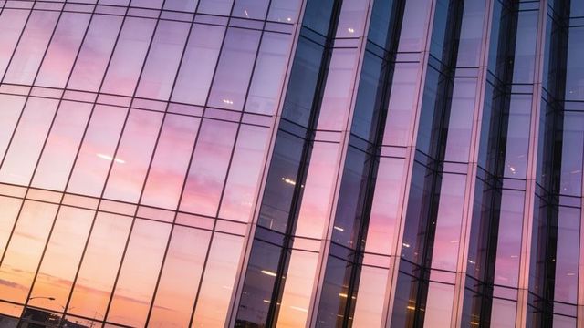 Glass office facade reflecting sunset colors with vertical fins and interior lights