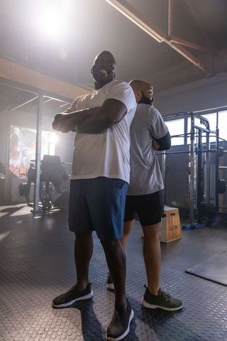 Two african men standing back-to-back in industrial gym celebrating strength and teamwork