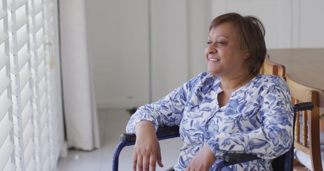 Elderly woman sits in wheelchair by window, smiling peacefully. Ideal for use in healthcare, senior care, and lifestyle content. Can be used in articles and advertisements focused on mobility aids, wellness, and home care.