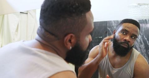 Man grooming beard with skincare product in modern bathroom