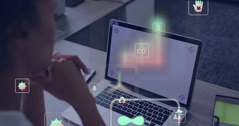 Mid-adult woman leaning over laptop interacting with holographic AR icons in modern workspace