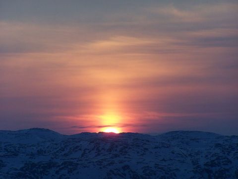 A beautiful winter sunset with the sun dipping below snowy mountain peaks, casting a serene light across the sky. Useful for backgrounds, landscape inspiration, nature blogs, travel websites, and romantic occasion graphics.