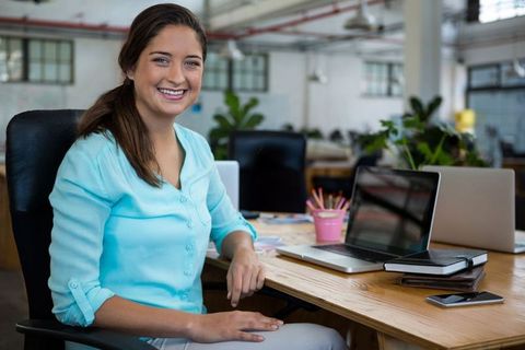 Smiling Professional Woman Using Laptop in Open-Plan Office