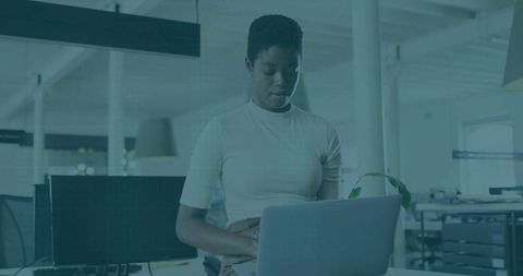 Professional woman standing and working on laptop in modern open-plan office with plant