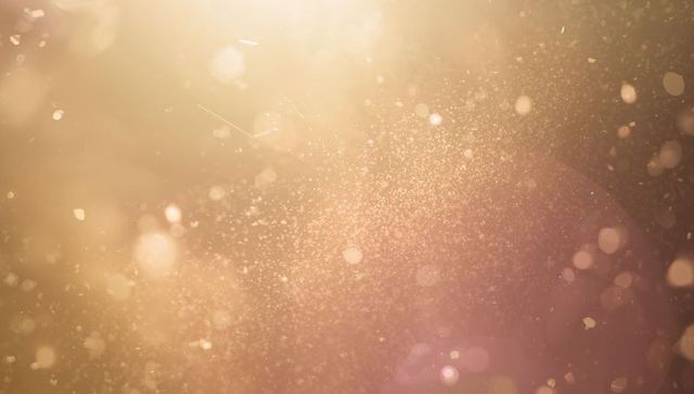 Golden dust particles drifting in warm backlight with soft bokeh and lens flare
