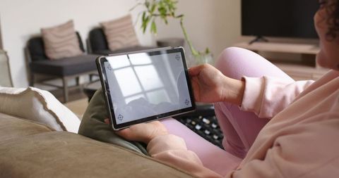 African american woman lounging on couch holding tablet showing window reflection
