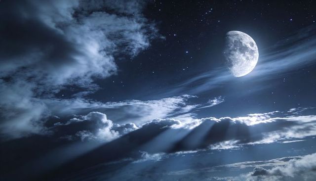 Moon casting silver beams over dramatic night cloudscape with stars and deep blue sky