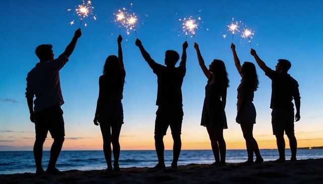 Friends holding sparklers on beach at dusk silhouettes celebrating summer together