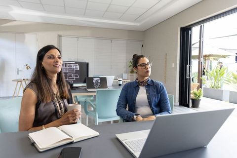 Two women discussing floor plans and blueprints in modern bright collaborative workspace