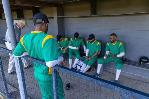 Baseball team relaxing in dugout wearing green uniforms preparing for game with coach